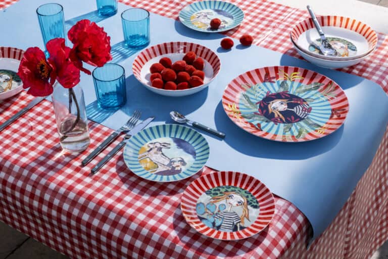 Olivia illustrated plates and bowls on a red gingham table with blue glasses and red poppies